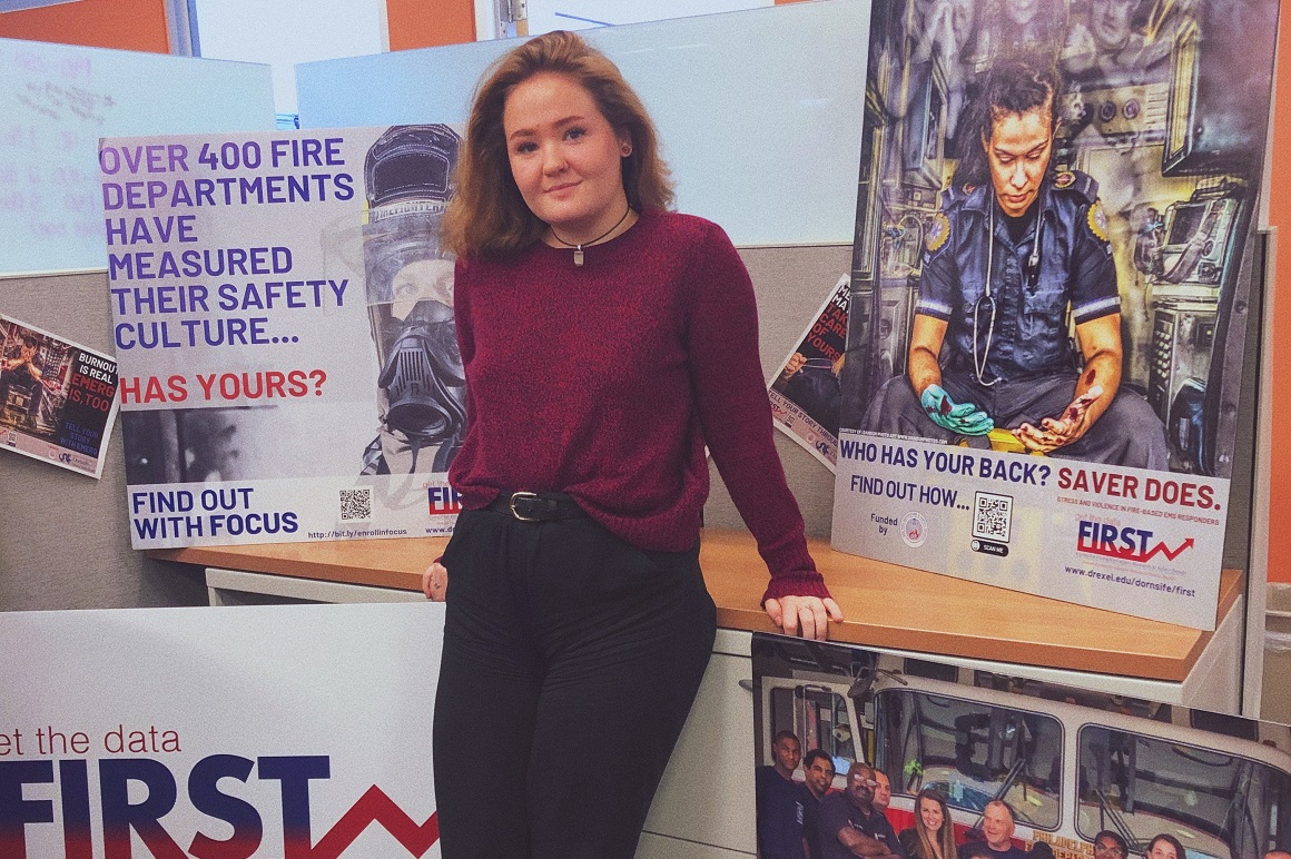 Victoria standing with FIRST Center posters